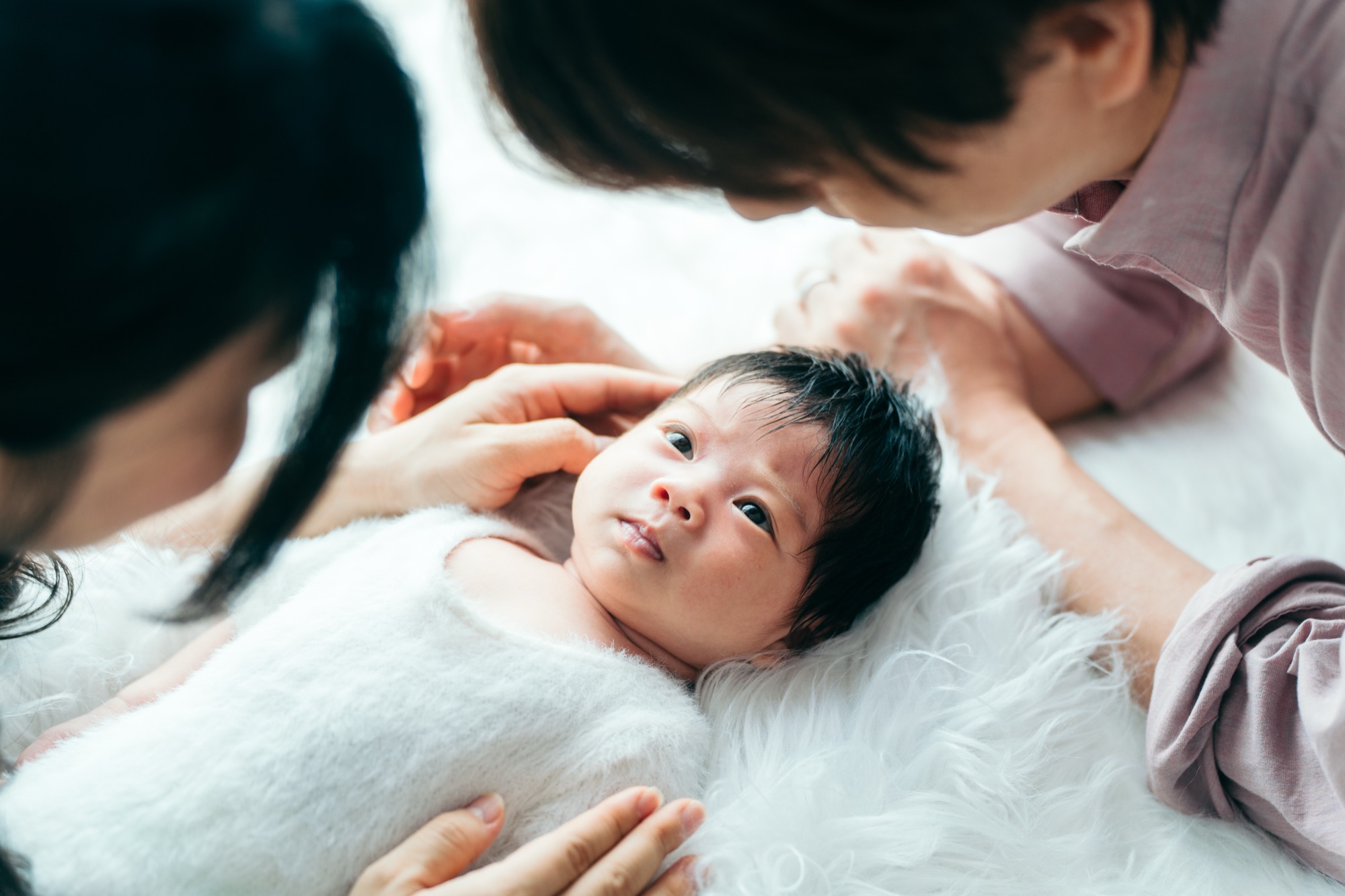 自宅ニューボーンフォトで白いファーの上の赤ちゃんをパパとママが覗き込むごろん俯瞰カット