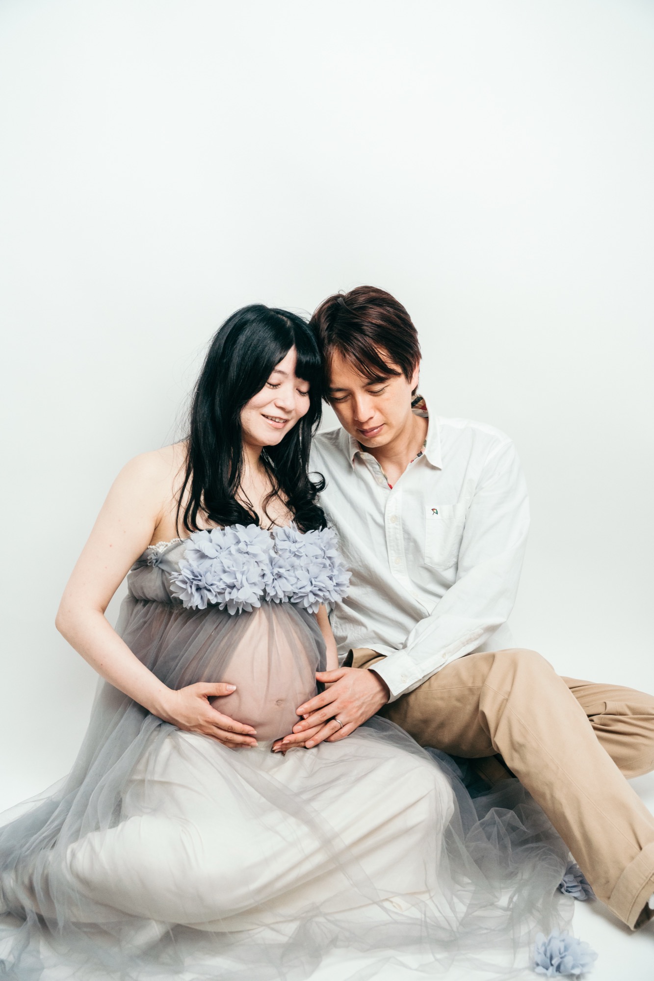 産後と比較するマタニティフォト:チュールドレスでおなかに手を添えて座るママと寄り添うパパ