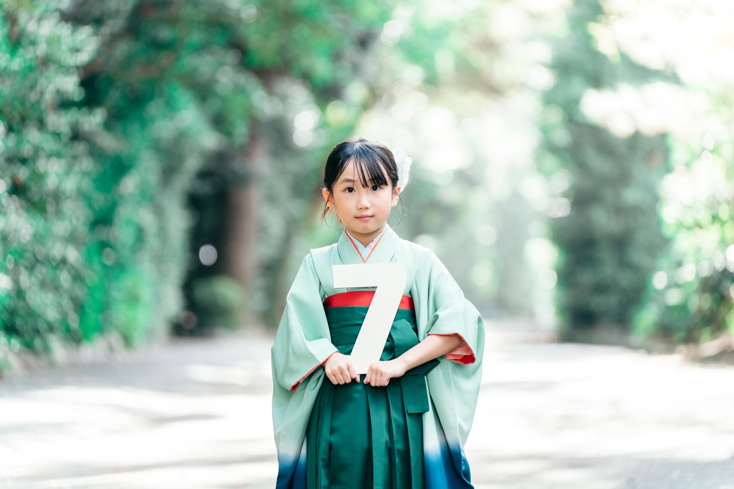 緑のトンネルで7のボードを持つ7歳の七五三