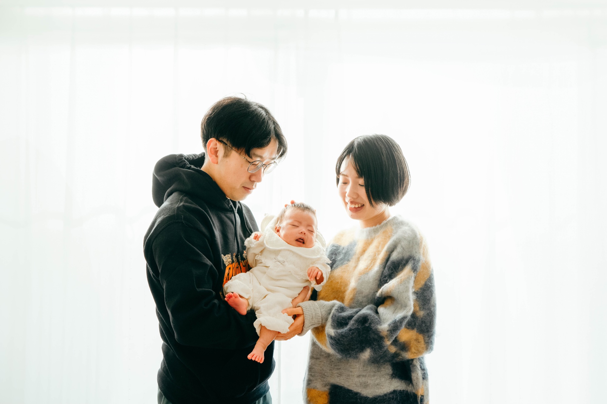 光あふれるリビングで赤ちゃんを抱くご夫婦の家族写真