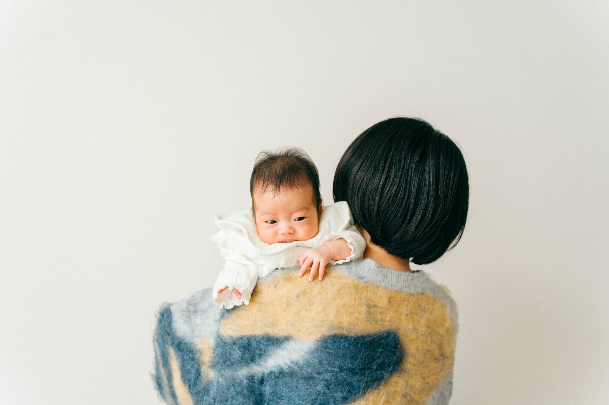 ママの肩越しにこちらを見る赤ちゃんの家族写真