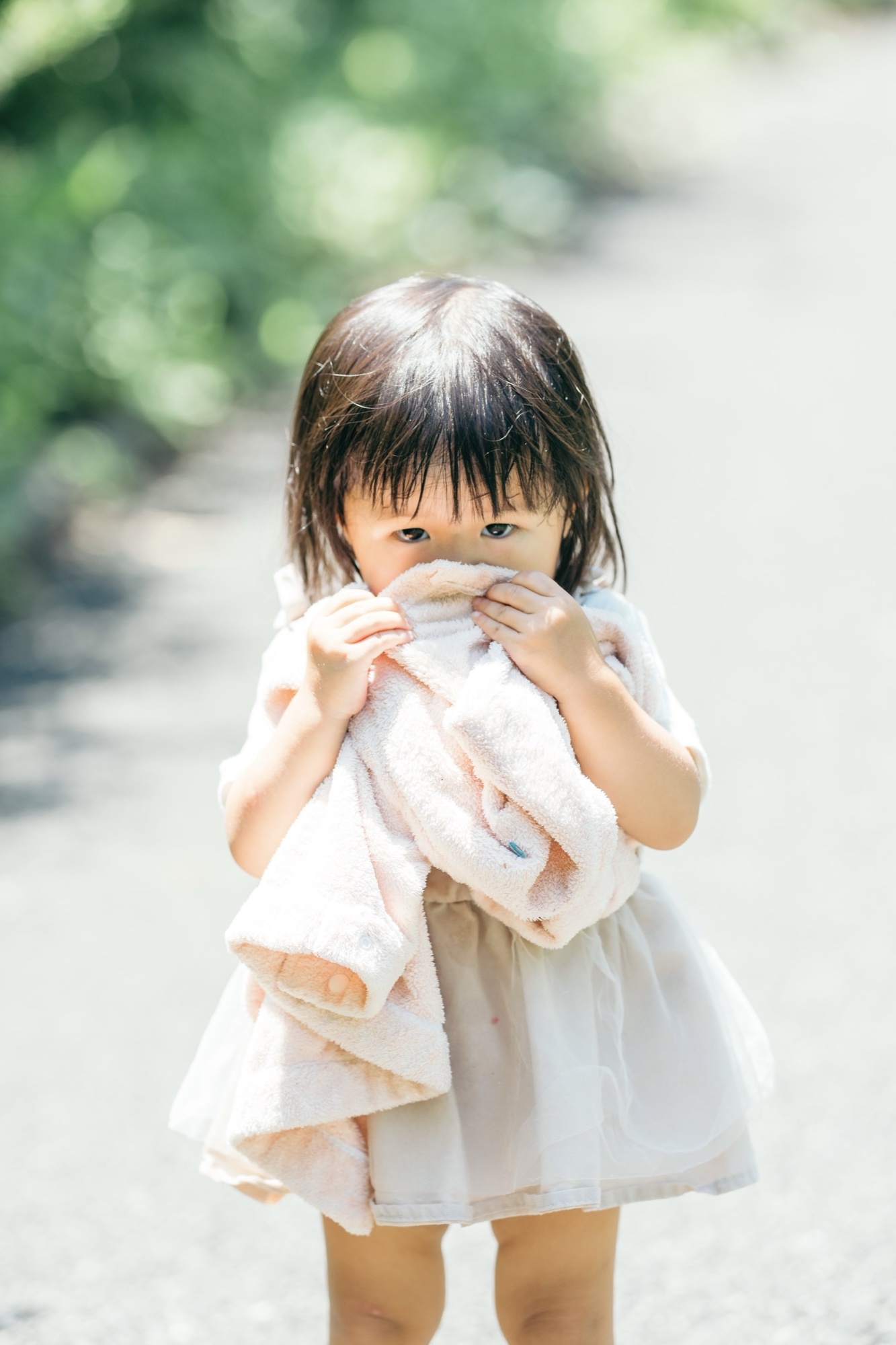 タオルを抱えて木もれ日のなかに立つ女の子の家族写真