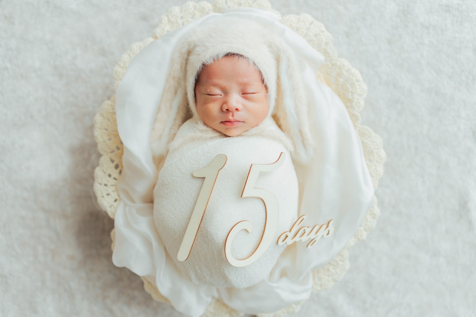 生後15日のニューボーンフォト。白いおくるみとうさぎのボンネットで眠る赤ちゃん