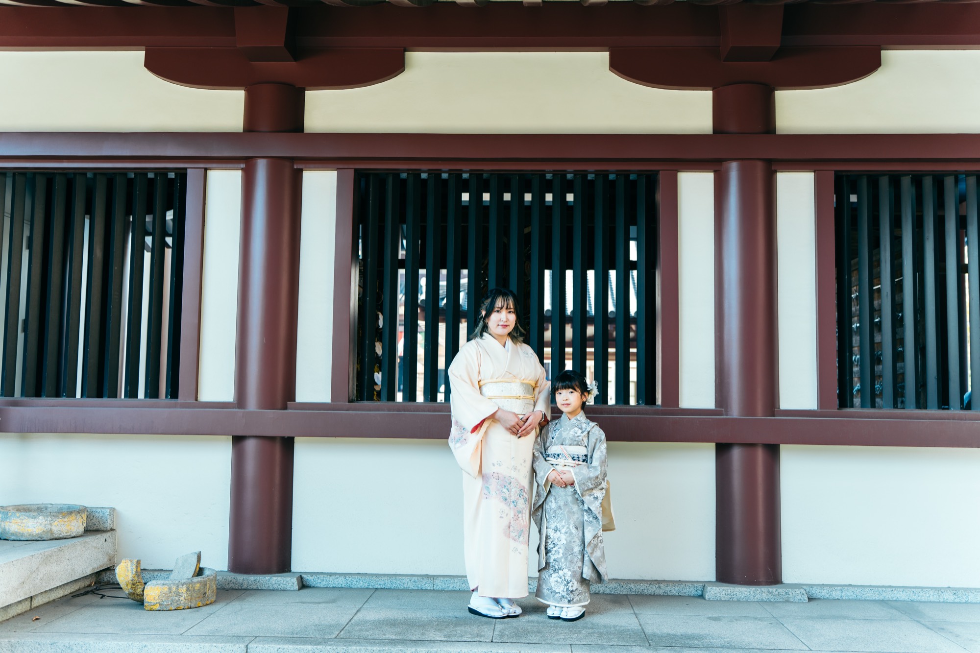 着物姿のお母様と並んで、川崎大師の社殿前に立つ七五三・7歳の女の子