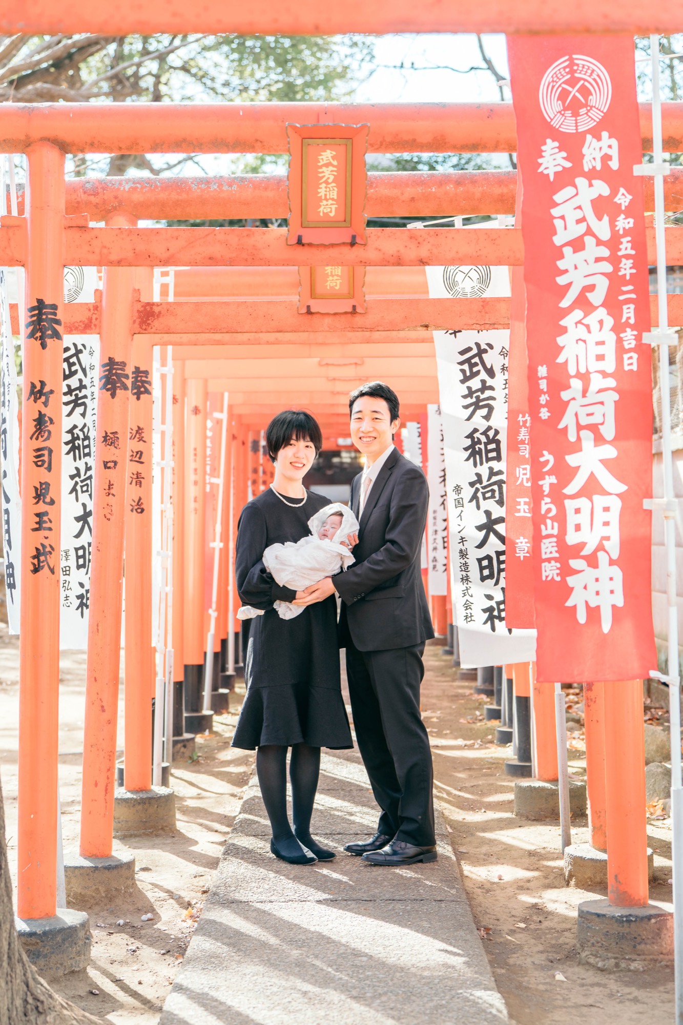 武芳稲荷の鳥居トンネルで撮影した、白い祝い着の赤ちゃんとご両親のお宮参り家族写真