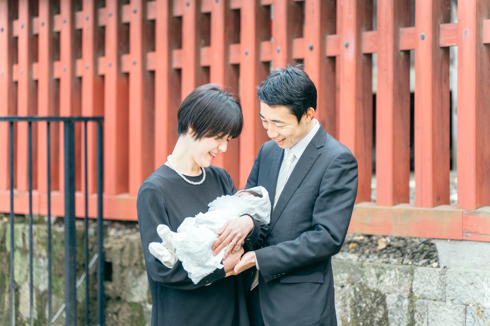 朱塗りの社を背景にお宮参りの赤ちゃんを抱くご両親(鬼子母神堂)