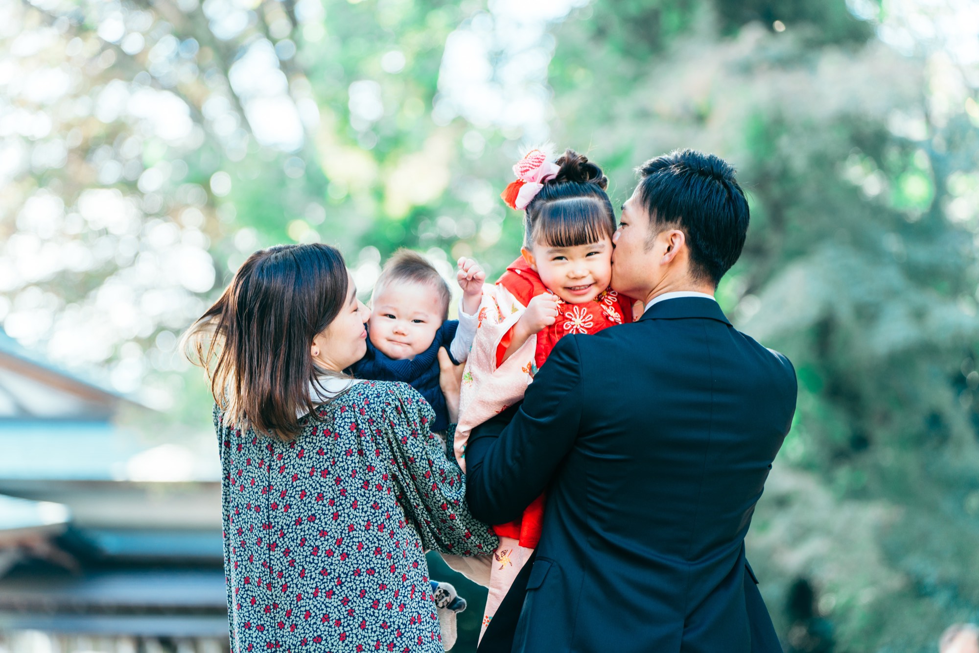 3歳の女の子と赤ちゃんの両頬に、パパとママがキスをする杵築大社の家族写真