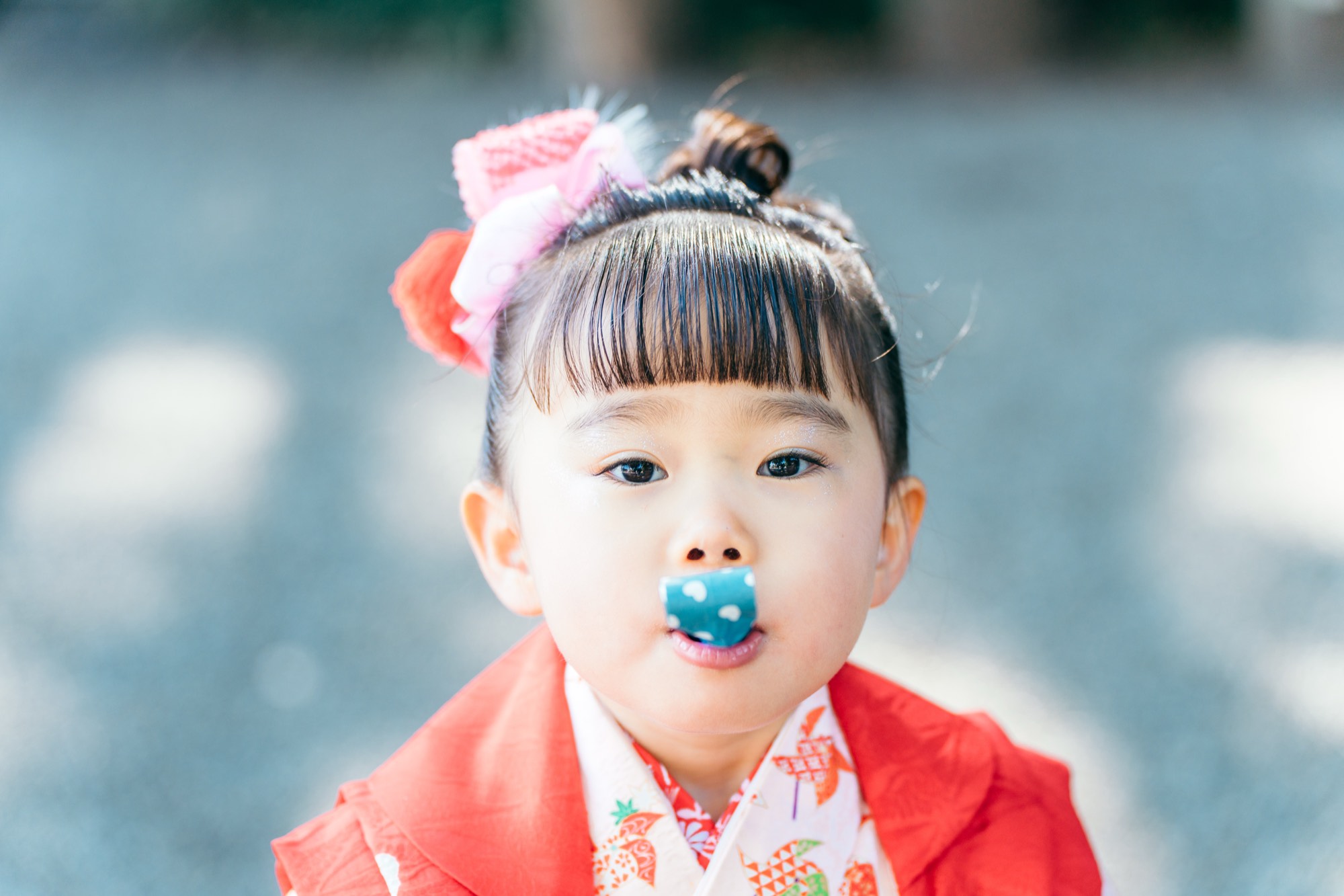 赤い被布姿で紙風船をくわえる、七五三・3歳の女の子(杵築大社)