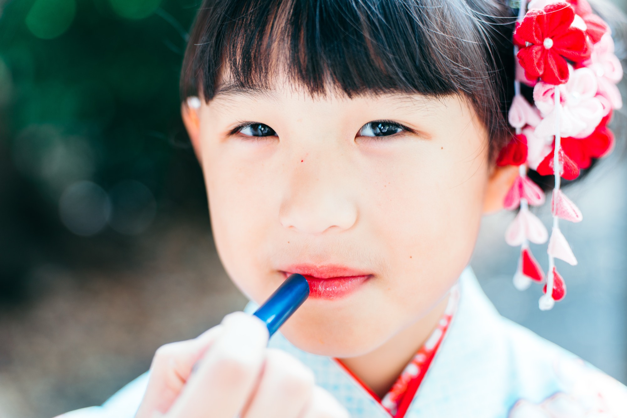 赤い髪飾りの七五三の女の子に口紅をのせる、お支度・ヘアメイクの様子