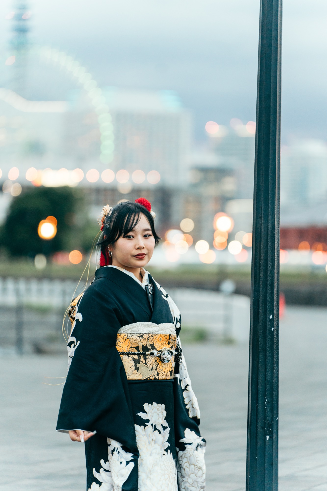夕暮れのガス灯のそばで、みなとみらいの灯りを背景に立つ黒振袖の成人式前撮り