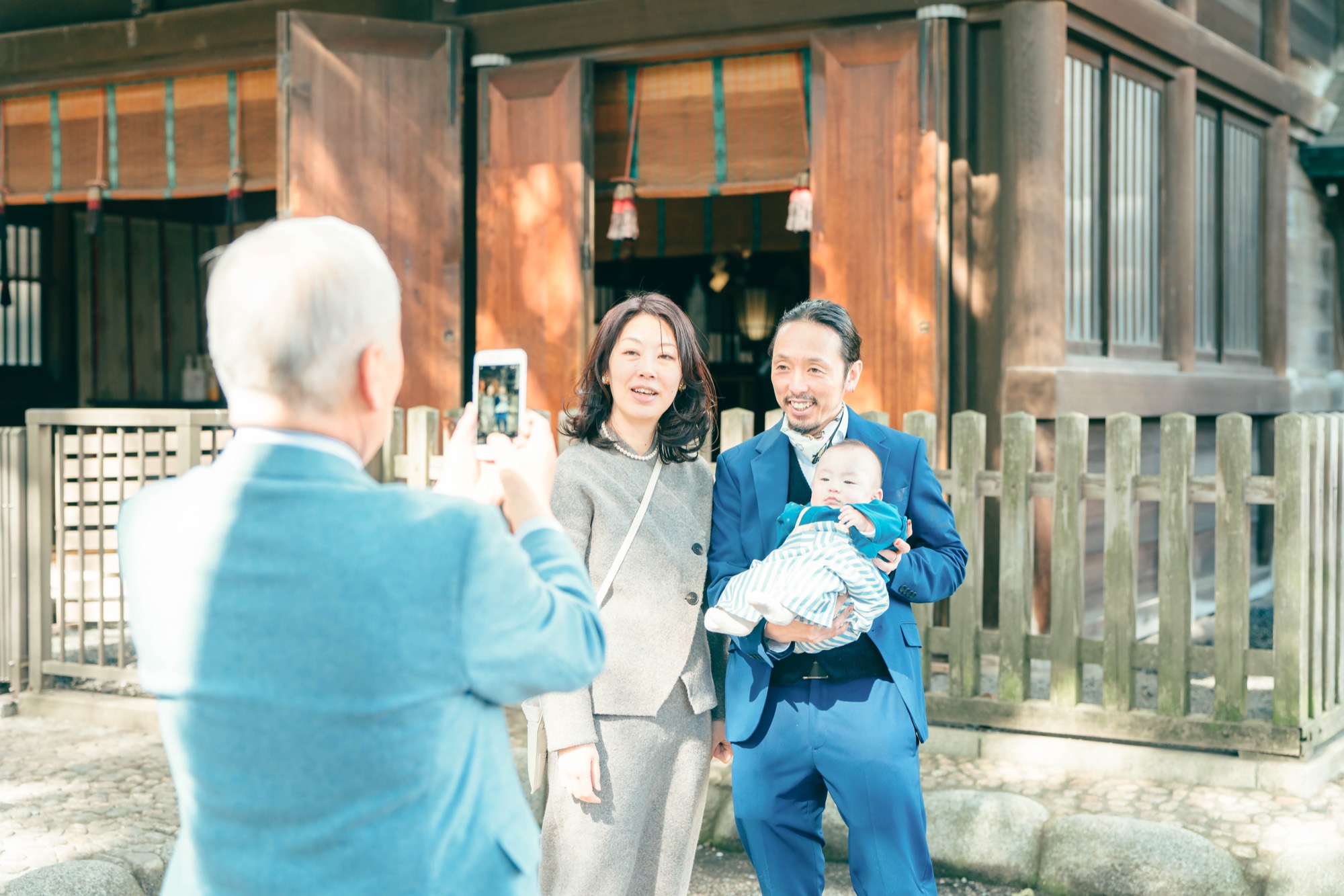 境内で赤ちゃんの様子を見守りながら写真を撮るおじいちゃん。お宮参りの和やかなひととき