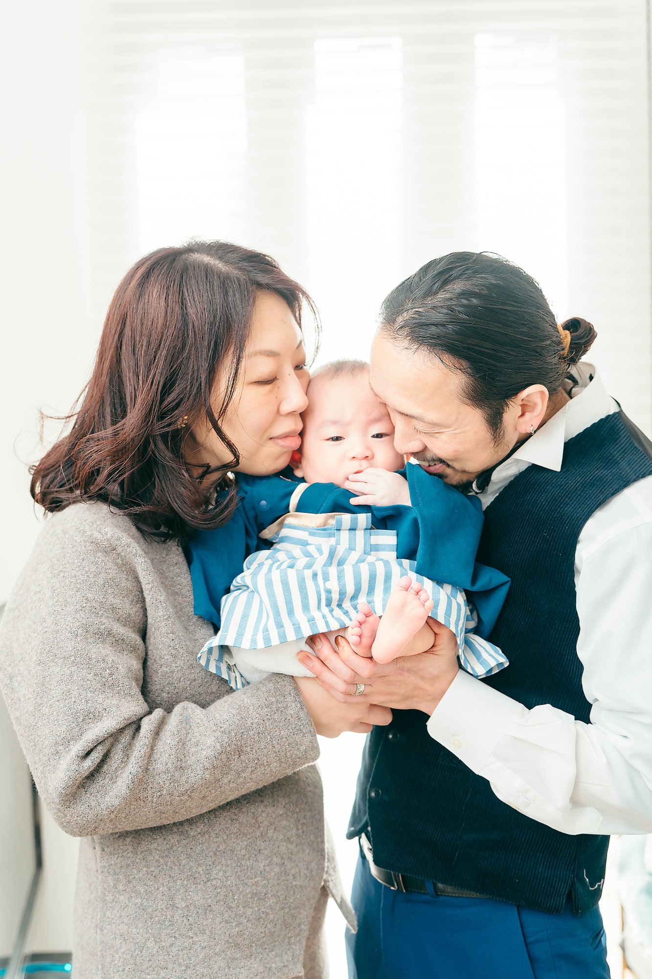 ご自宅で、赤ちゃんの頬に両側からそっと顔を寄せるパパとママ。お食い初めの記念に