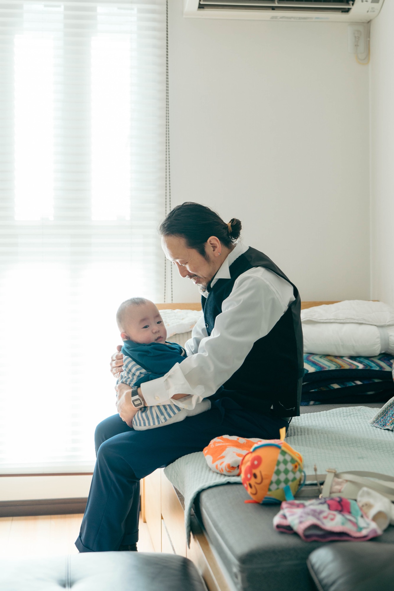 明るい光の差し込むお部屋で、赤ちゃんを抱いて見つめるパパ。お宮参り・お食い初めの一日