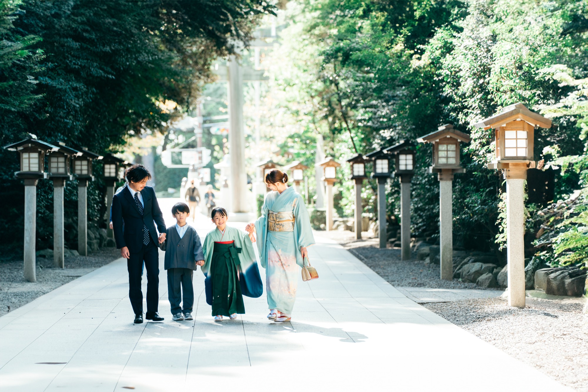 寒川神社の灯籠が並ぶ参道を歩く七五三の家族（袴姿の7歳の女の子・着物姿のお母様・お兄ちゃん・お父様）
