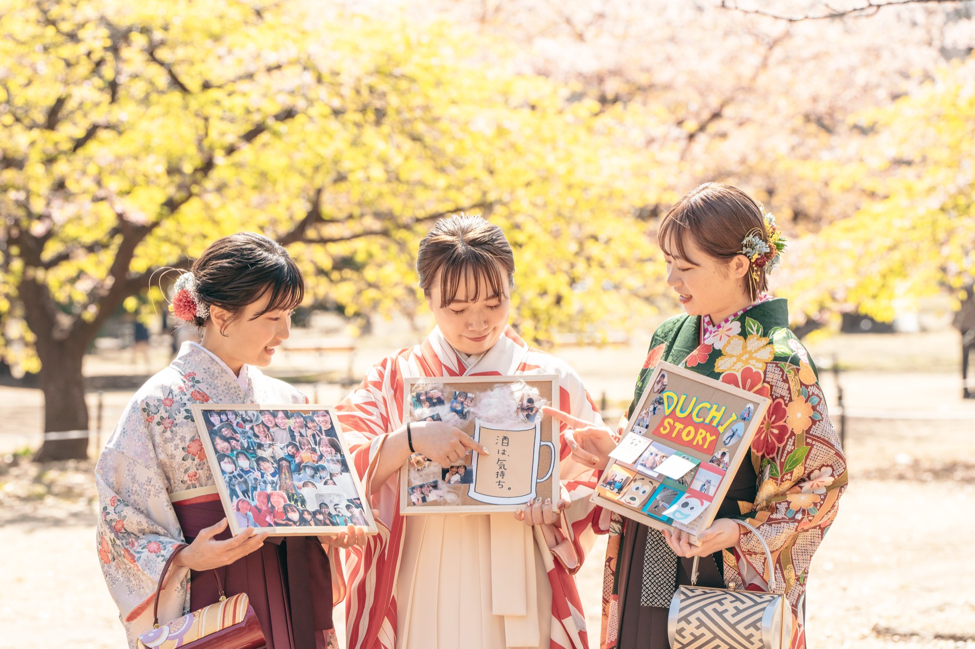 桜の咲くなか、卒業アルバムを開いて思い出を振り返る袴姿の卒業生たち