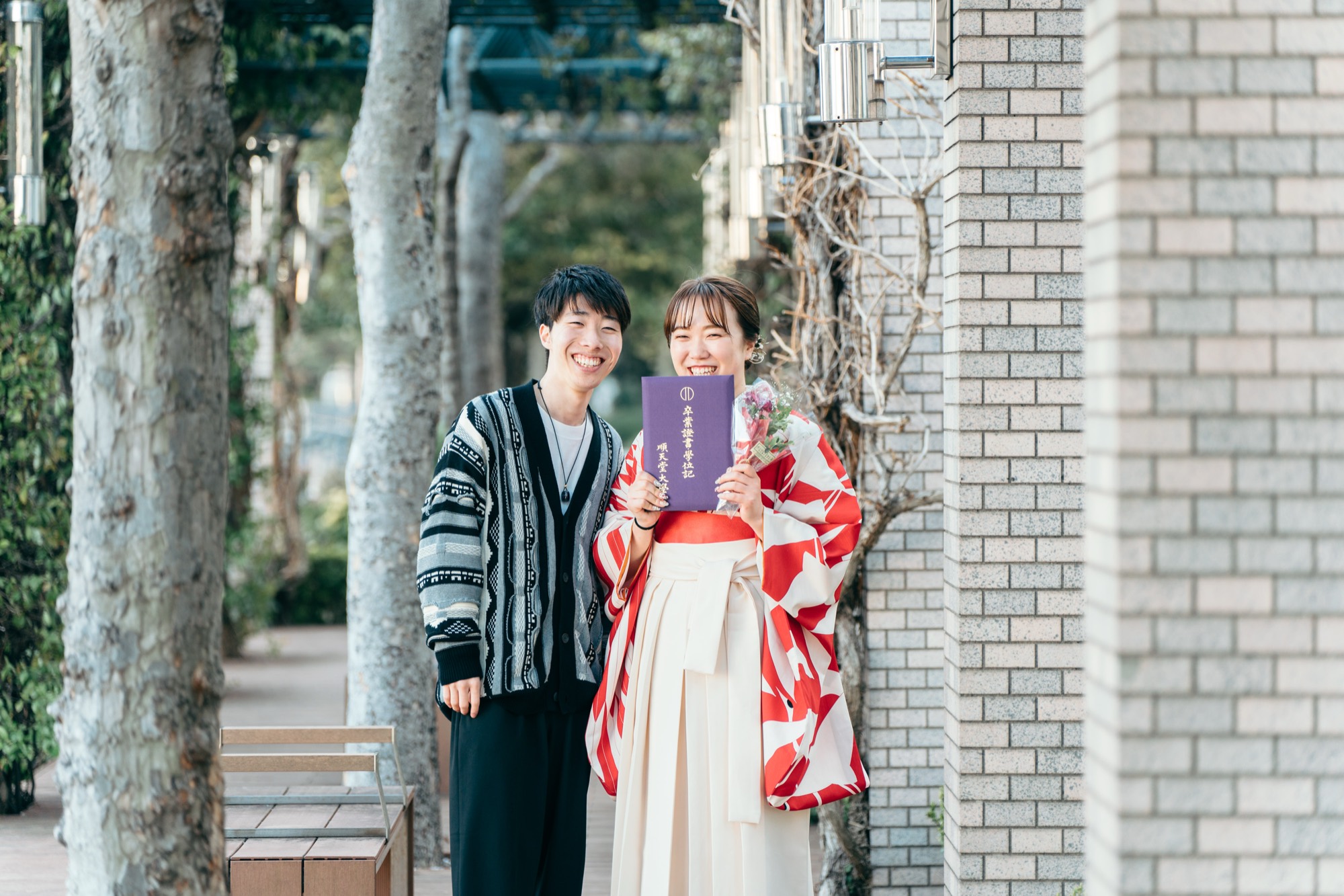 卒業証書を手に、袴姿の卒業生と恋人が並んで笑う記念写真