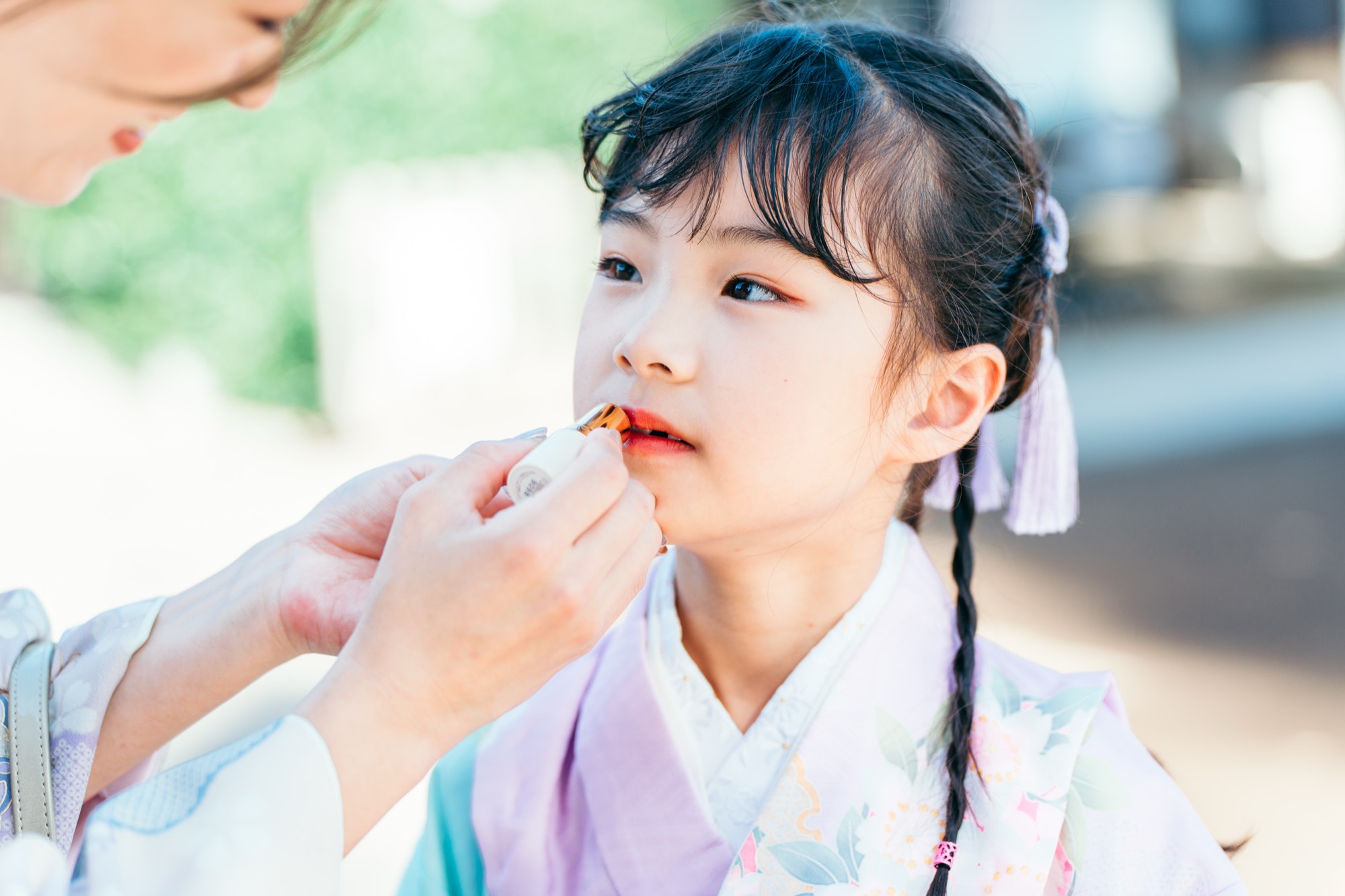 パステルの着物姿の7歳の女の子に口紅をのせる、七五三のお化粧の様子