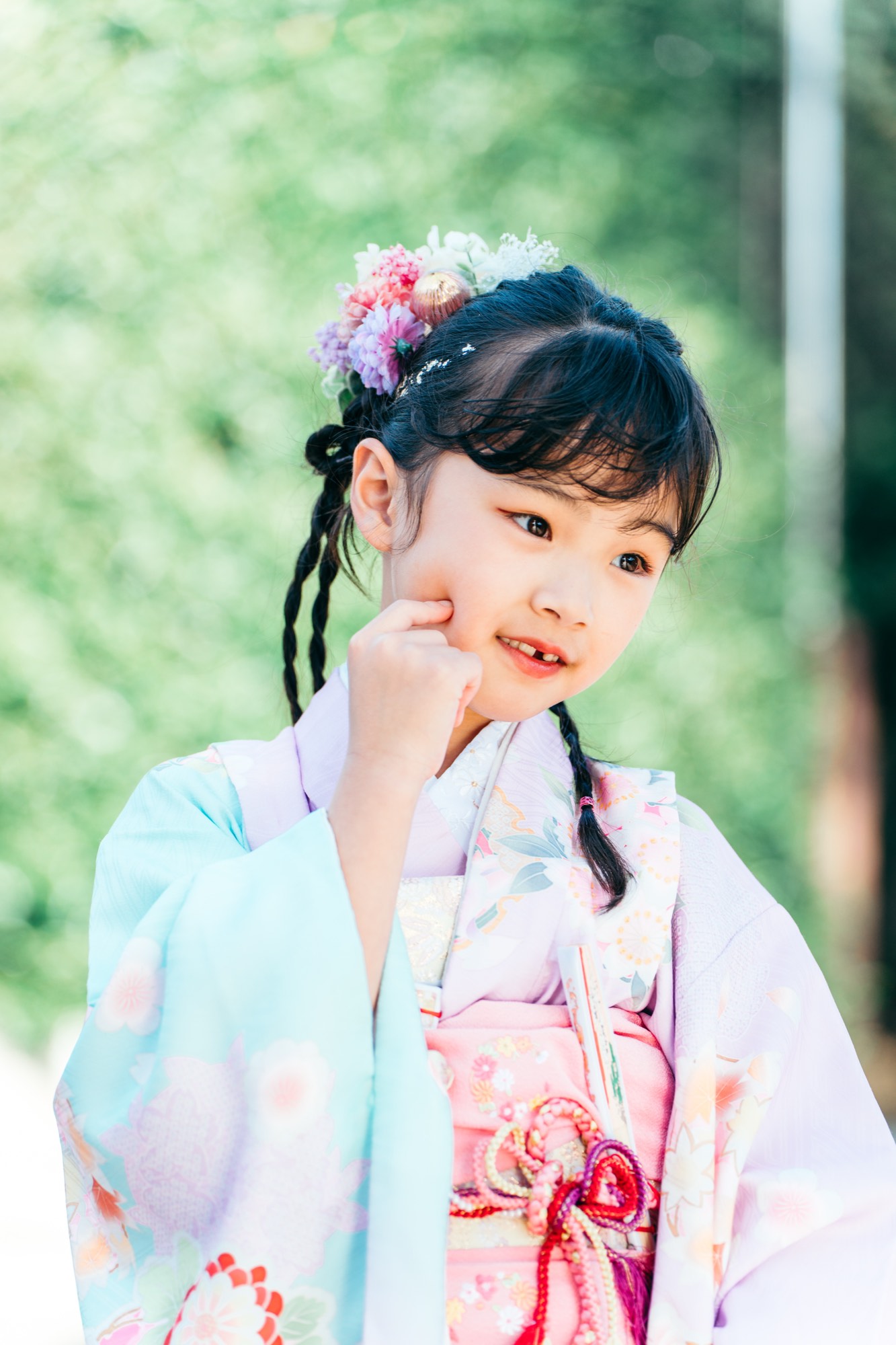 緑をやわらかくぼかした背景に立つ、パステルの着物姿の七五三・7歳の女の子